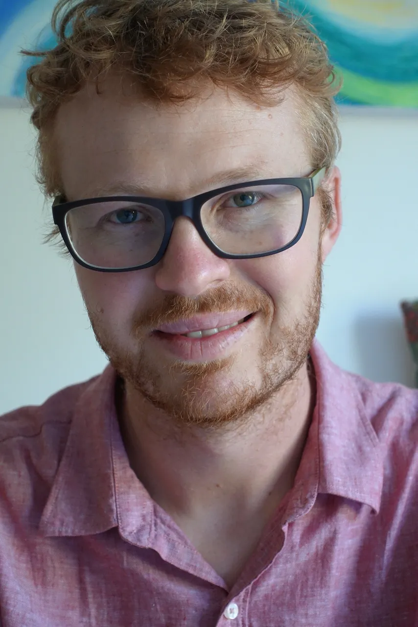 Ben headshot with a pink shirt and artwork in the background